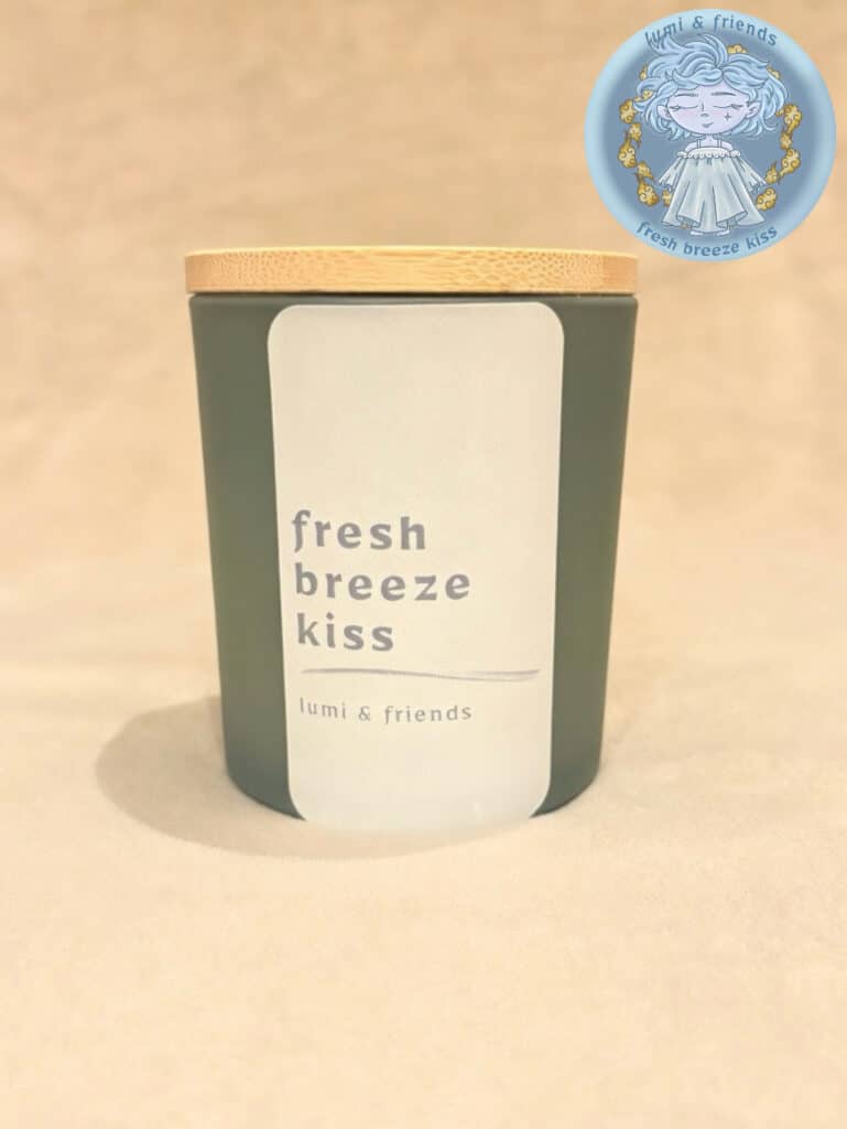 duftlys, matgrønt glas med bambuslåg og pastel blå label. tekst med fresh breeze kiss, duftlys med duft af friske jasminblomster, kokosmælk og tropiske frugter i sommerluft. billede i højre top hjørne af karakter til lyset, bia breeze, let og luftig eventyrlig tegnet figur.